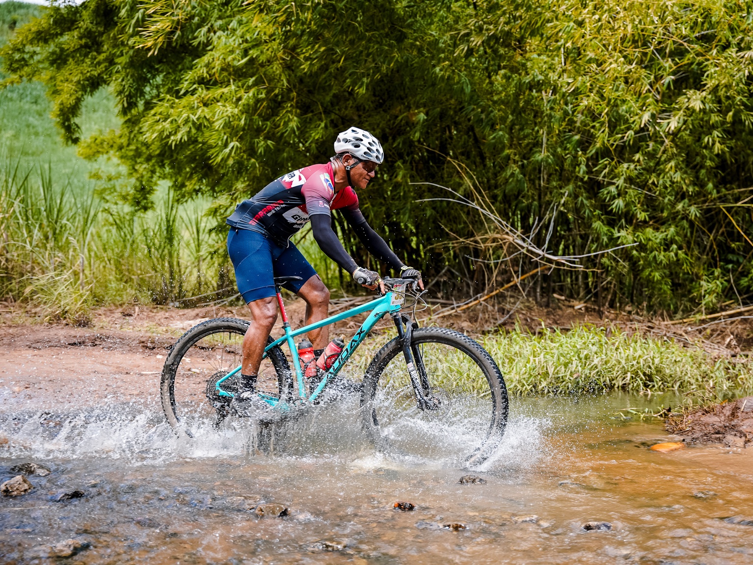 Ciclista em uma bicicleta verde atravessando um riacho junto à mata.